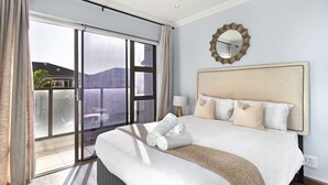 Quarto de hotel com uma cama grande, vista através de uma porta de vidro deslizante e um espelho redondo na parede.