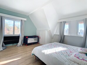 Ein Schlafzimmer mit Etagenbett, einem großen Bett mit gemusterten Textilien und Blick auf Bäume durch die Fenster.