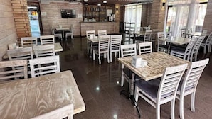 Interior de restaurante com vigas de madeira no teto, piso de azulejos e várias áreas de estar.