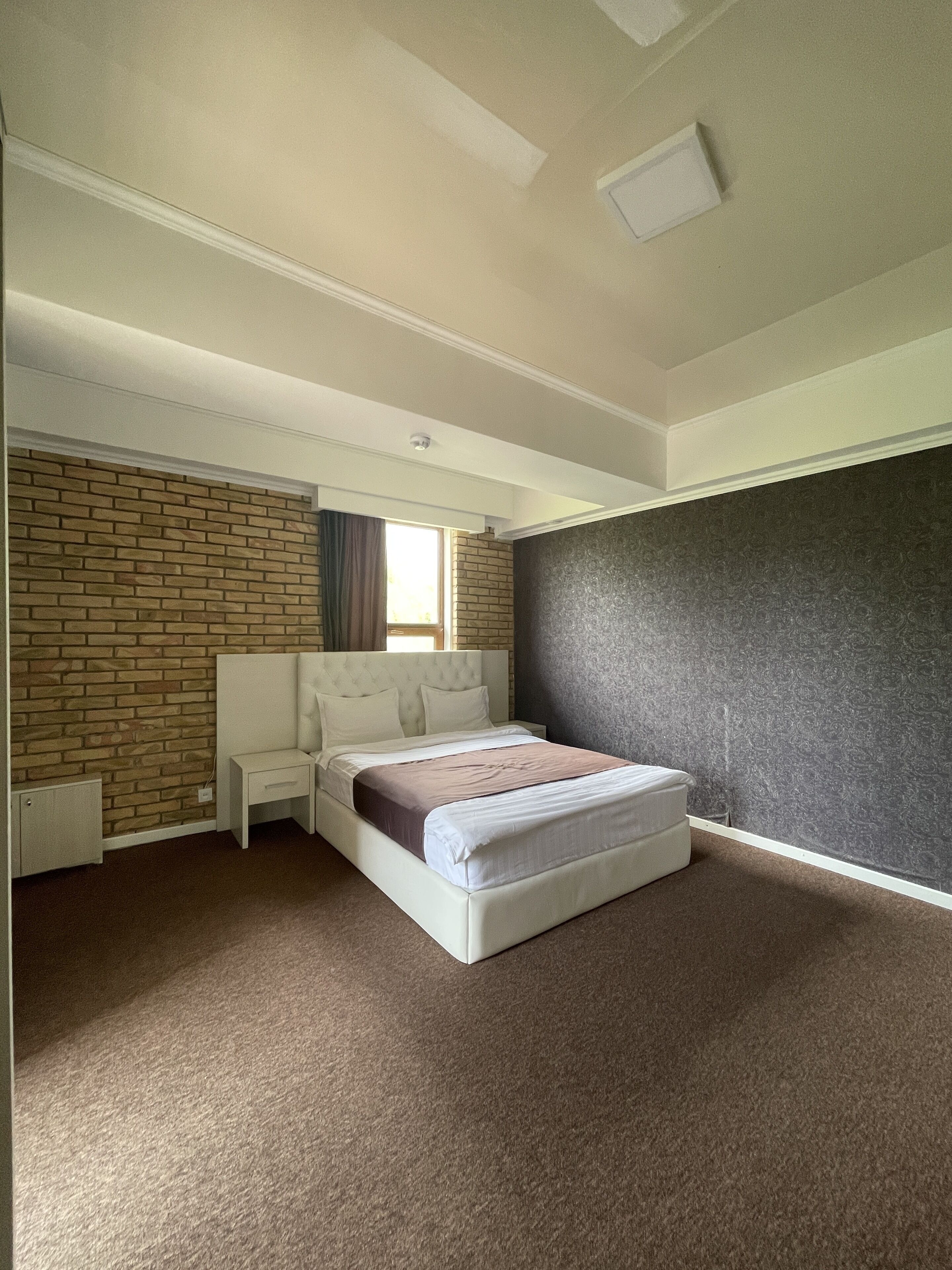 A bedroom with a brick-patterned wall, a white bed, and a dark textured wall.