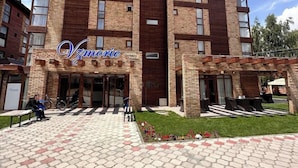 Um hotel com fachada de tijolos, entrada central e um pátio pavimentado com áreas de estar.