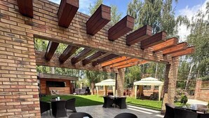 Um pátio externo com paredes de tijolo, pérgola de madeira e mobiliário de exterior.