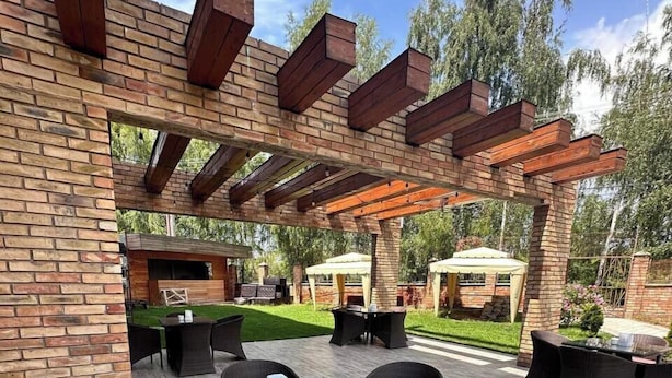 Eine Terrasse im Freien mit Backsteinmauern, einer Holz-Pergola und Gartenmöbeln.