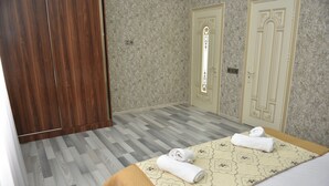 A hotel room with a wooden wardrobe, two doors, a patterned bedspread, and a rolled towel on the bed. - Foothills villa (Gabala)