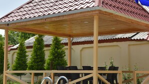 A covered outdoor seating area with a pool, wooden deck, and chairs. - Foothills villa (Gabala)