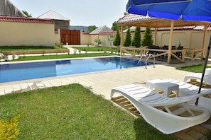 A swimming pool with lounge chairs and a covered seating area.