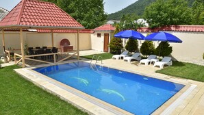 A swimming pool with a red-roofed pavilion, lounge chairs, and a covered patio area. - Foothills villa (Gabala)