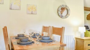 A dining table set with plates, bowls, and glasses, surrounded by wooden chairs. - The Studio at Malt Kiln Cottage (Grizebeck, near Kirkby-in-Furness)