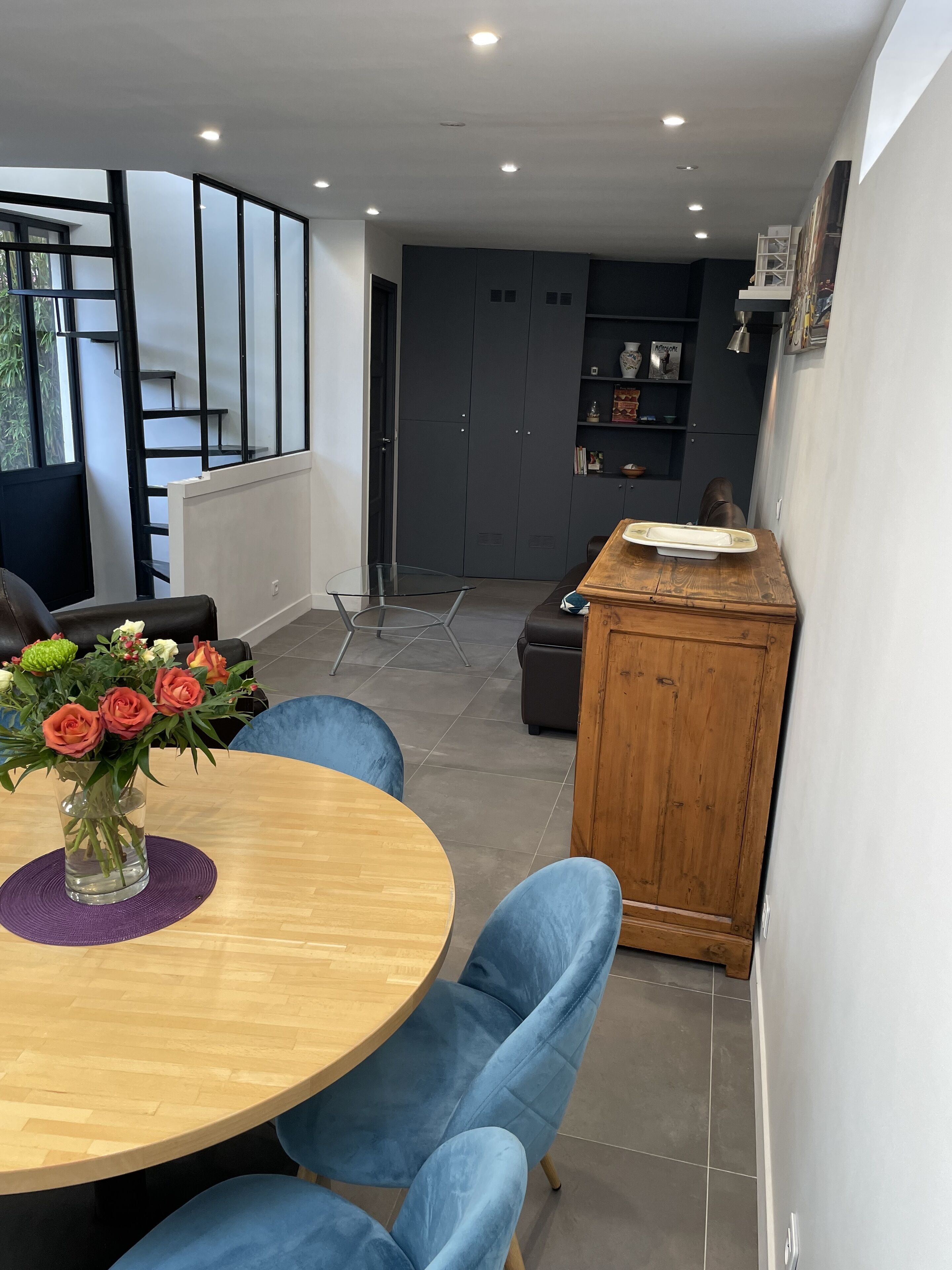 Un espace repas moderne avec une table ronde en bois, des chaises à revêtement bleu et un vase rempli de fleurs.