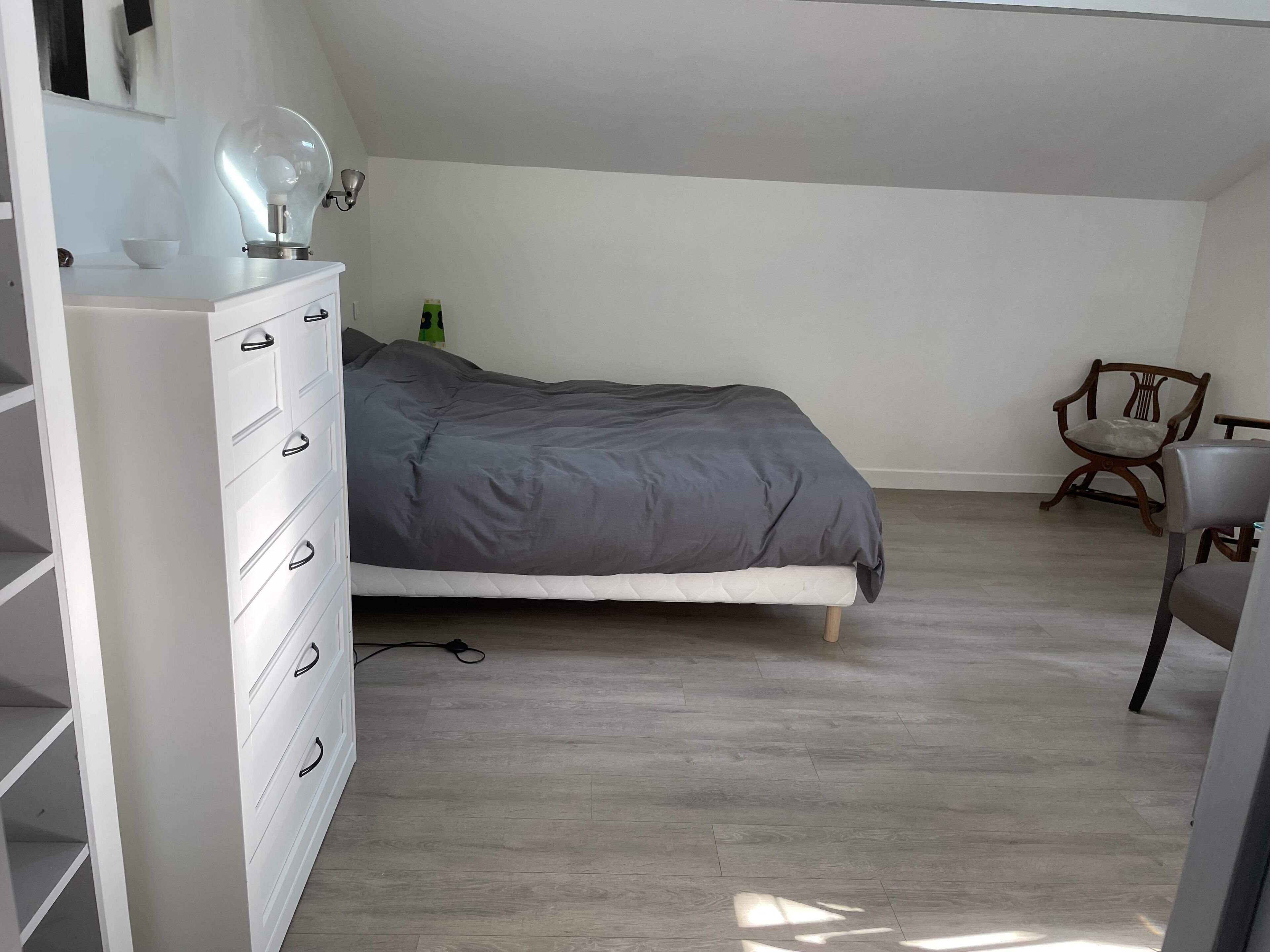 Una camera da letto con un letto, una cassettiera, una sedia e una lampada.