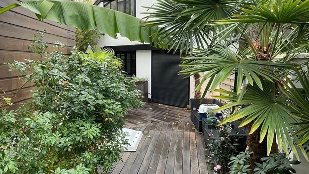 Une terrasse en bois agrémentée de plantes en pot et une porte de garage noire.