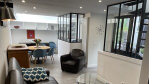 Un salon moderne avec un canapé en cuir, une table basse en verre et un coin repas comprenant une table en bois et des chaises bleues.