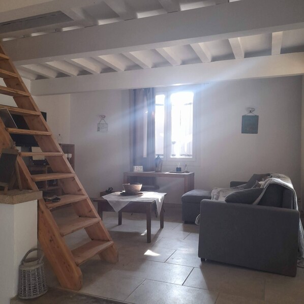 A living room with a wooden staircase, a table with a basket, a sofa, and a window with curtains. - Charmante Maison de Campagne Arborée Avec Piscine (Sanilhac-Sagriès)