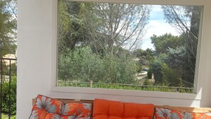A window seat with orange cushions and a yellow cushion, overlooking a garden with trees and a fence.