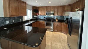 A modern kitchen with wooden cabinets, a stainless steel refrigerator, a microwave, and a stove. - Penthouse in Paradise! (Key West)