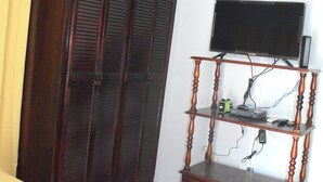 Une chambre à coucher avec un lit, une armoire, un téléviseur posé sur un meuble en bois et un ventilateur de plafond.