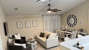 Un salon spacieux avec un canapé blanc, un fauteuil noir et un coin repas comprenant une table et des chaises.