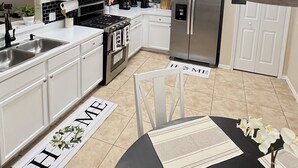 Une cuisine moderne avec des meubles blancs, un réfrigérateur en acier inoxydable et une table à manger noire agrémentée d’un set de table.