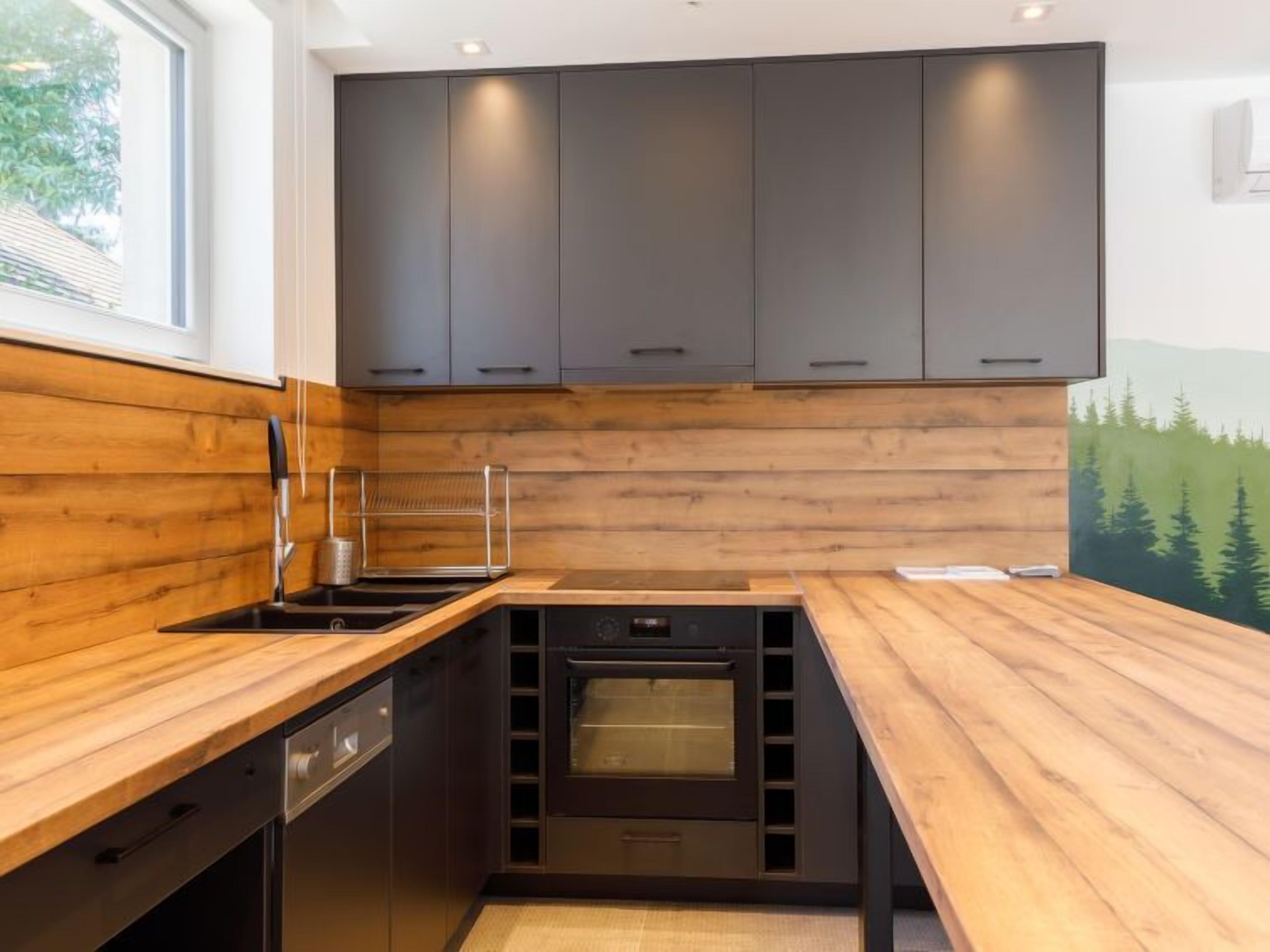 Eine moderne Küche mit dunklen Schränken, einer Holz Arbeitsplatte, einem eingebauten Backofen und einem Fenster mit Blick auf Bäume.