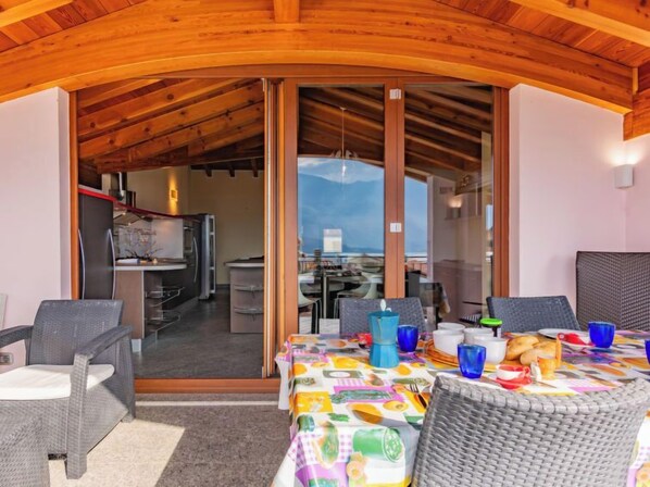 A dining area with wicker furniture, a colorful tablecloth, and a view of a kitchen and dining area through glass doors.