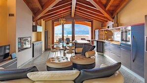 A spacious living area with a high ceiling and wooden beams, a dining area with a view, and a modern kitchen with stainless steel appliances.