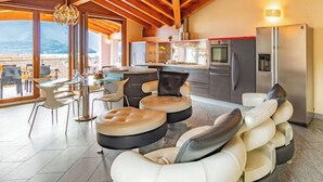 A modern kitchen with stainless steel appliances, a dining area with a glass table and chairs, and a seating area with cushioned chairs.