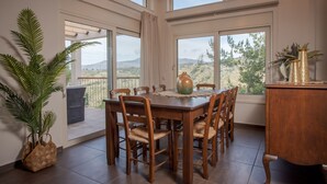 Un coin repas avec une table et des chaises en bois, de grandes fenêtres offrant une vue sur le paysage, une plante en pot et un vase décoratif.