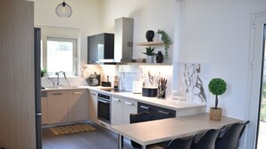 Une cuisine moderne avec un dosseret en marbre, des appareils en acier inoxydable et un coin repas doté de chaises noires.
