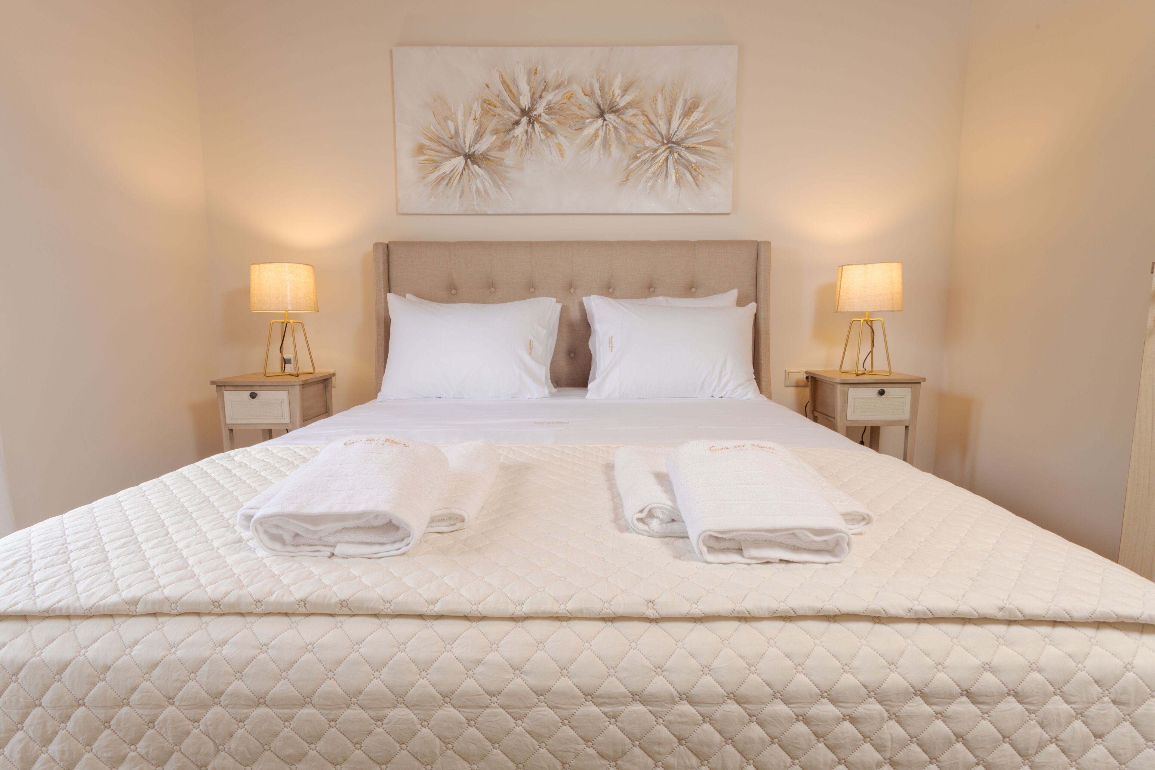A neatly made bed with two towels, a headboard, and two bedside lamps.
