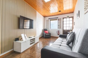 A modern living room with a flat-screen TV, a grey sofa, a small armchair, and a wooden slatted wall.