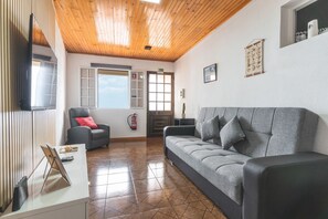 A modern living room with a wooden ceiling, a grey sofa, a grey armchair, a flat-screen TV, and a fire extinguisher. - Casa Moreira by Atlantic Holiday (Caniçal)