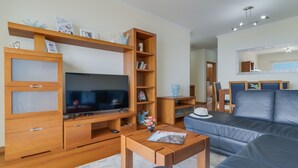A modern living room with a flat-screen TV, wooden entertainment unit, a sofa, and a dining area with a table and chairs.
