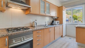 A modern kitchen with wooden cabinets, a stainless steel stove, and a window with a view of a hillside.