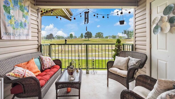 A covered porch with wicker furniture, a view of a golf course, and decorative string lights. - Home on the Golf Range - Holiday Hills Branson - Golf Resort - Outdoor Pools (Branson)