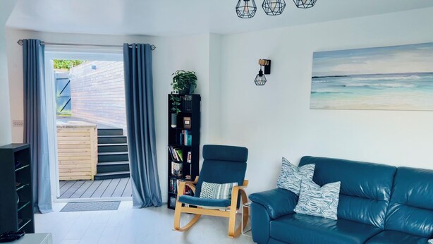 Una sala de estar moderna con un sofá de cuero azul, un sillón mecedor de madera, una estantería negra y un ventanal con cortinas.