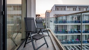 A balcony with two chairs, a glass railing, and a view of a modern building with multiple floors. - Ria Apartments (Navodari)