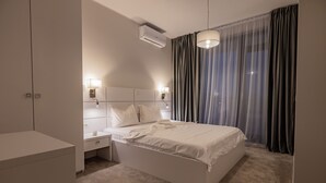 A modern bedroom with a large bed, bedside lamps, an air conditioner, and a view through sheer curtains. - Ria Apartments (Navodari)