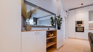 A modern kitchen with white cabinetry, a large mirror, a bowl of fruit, and a potted plant. - Ria Apartments (Navodari)
