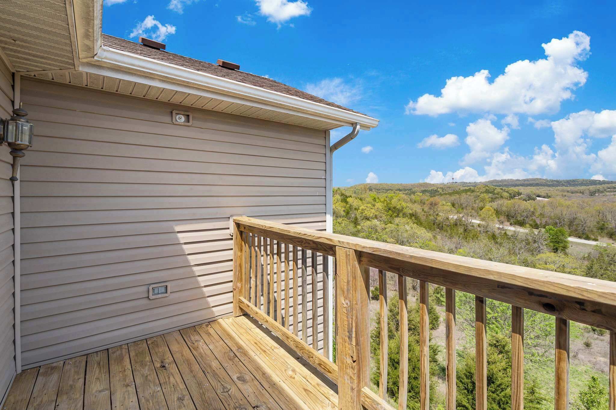 A wooden deck with a railing, a light fixture, and a view of a hilly landscape.