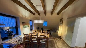 A modern kitchen with wooden cabinets, a dining area with a table and chairs, and a large window with curtains. - Cozy apartment 2 in the DG in the Sonnenhof (Dippoldiswalde)