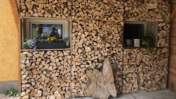 A rustic cabin interior with a stone wall built from stacked firewood, two windows with flower boxes, and a large rock centerpiece. - Cozy apartment 2 in the DG in the Sonnenhof (Dippoldiswalde)