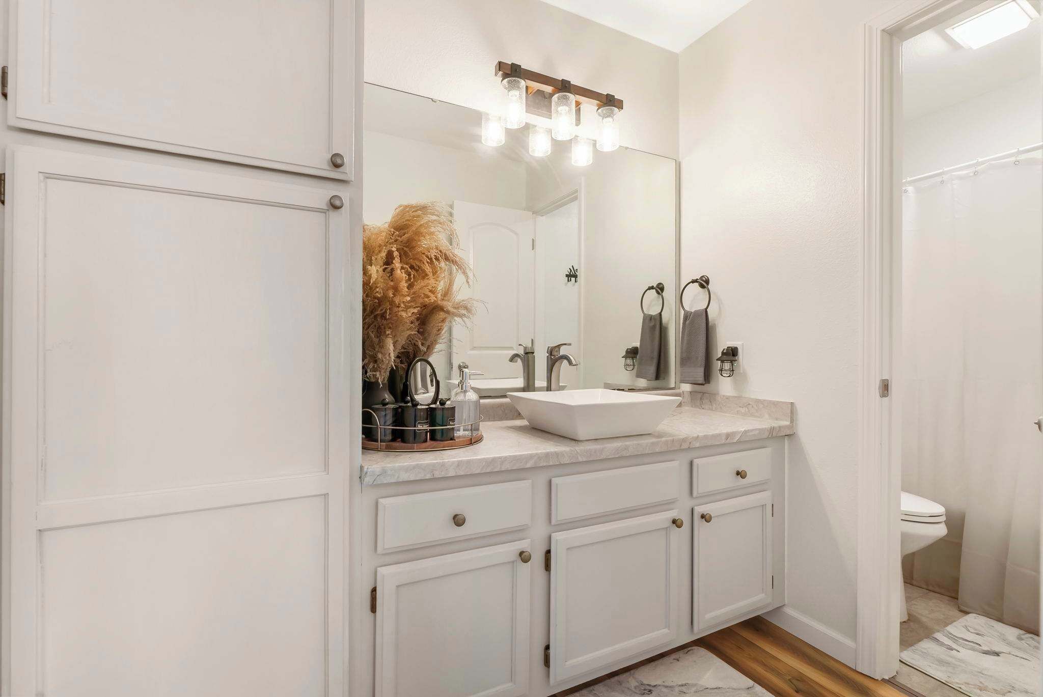 A bathroom with a white vanity, a large mirror, and a light fixture above the mirror.