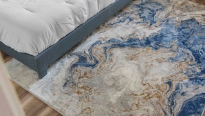 Ein Bett mit grauem Gestell und weißer Bettwäsche, ein Teppich mit Marmormuster und Holzböden.