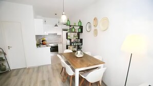 A modern kitchen with white cabinets, a wooden dining table, and white chairs. There is a small island with a sink and a fruit bowl. - Isa SkyHouse Algarve (Portimão)
