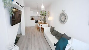 A modern living room with a white sofa, a dining table, and a kitchen area in the background. - Isa SkyHouse Algarve (Portimão)