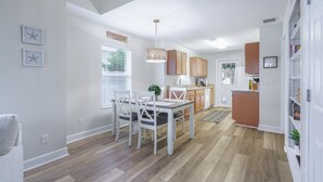 Una cocina moderna con armarios blancos, un comedor con mesa y sillas, y una pequeña isla con un lavamanos.