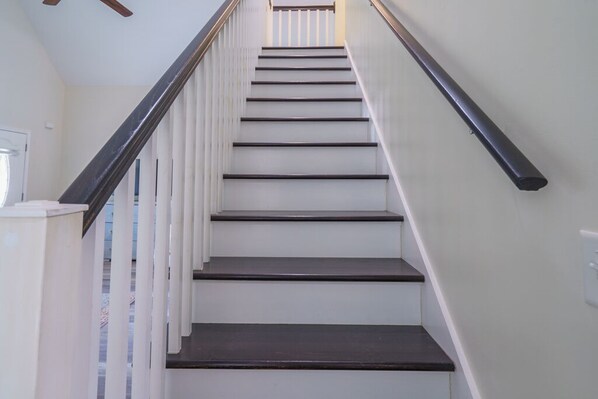 A staircase with white walls and dark steps, leading to a landing with a ceiling fan.