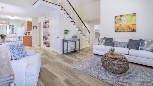 Un salón amplio con una escalera, un conjunto de sofá blanco, una mesa de centro y un cuadro en la pared.