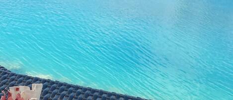 A view of a clear blue pool with a lounge area in the foreground.