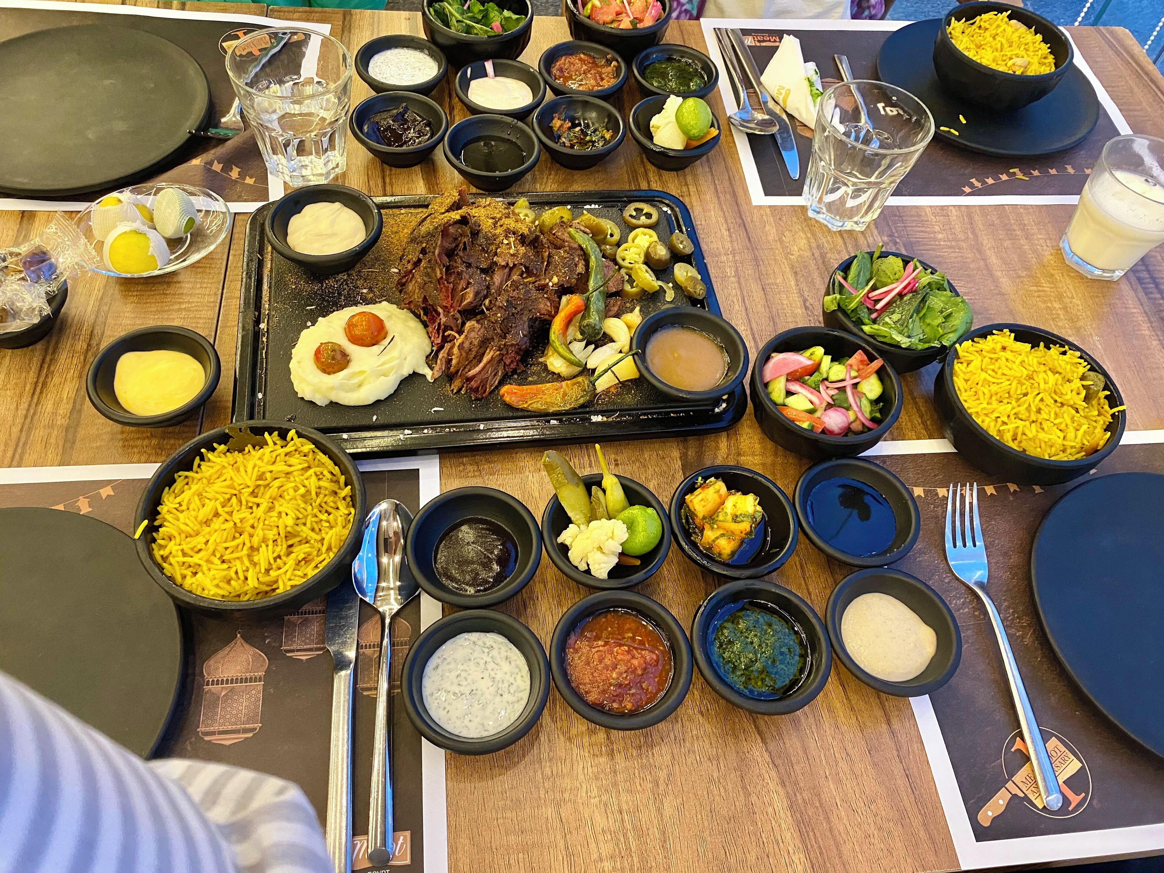 Una mesa servida con diversos platos, incluyendo arroz, carne y varios recipientes pequeños con salsas y aderezos.